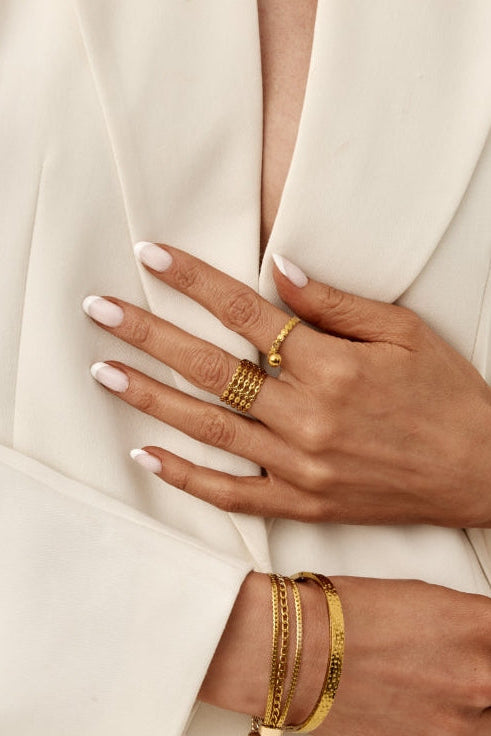 Close-up of hands wearing gold jewelry on a neutral background